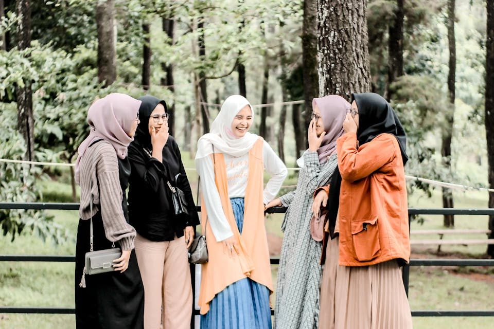 Five women in hijabs laughing and enjoying time together in an outdoor forest setting.