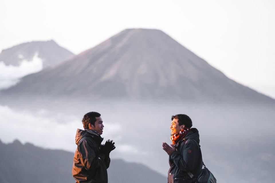 Asal Usul Nama Desa Gumeng dan Wisata Alam Lereng Gunung Lawu Two men enjoy a scenic hike on Indonesia's Gunung Prau, surrounded by misty mountains at sunrise.