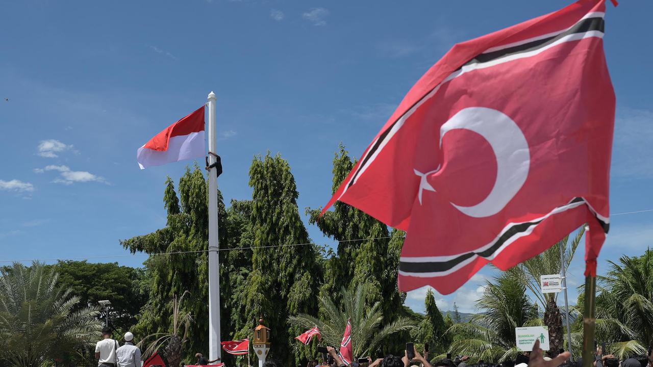 Seorang pria memanjat tiang bendera untuk mengibarkan bendera Bulan Bintang berdampingan dengan bendera Merah Putih di halaman Masjid Raya Baiturrahman Banda Aceh saat peringatan 21 tahun Hari Damai Aceh 15 Agustus 2026, terkait dengan hubungan Aceh dan Indonesia.